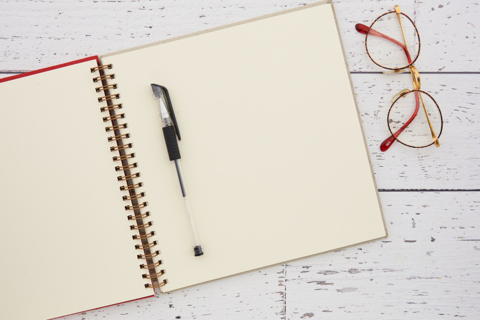 Cuaderno abierto junto a unas gafas y un bolígrafo sobre una mesa de trabajo