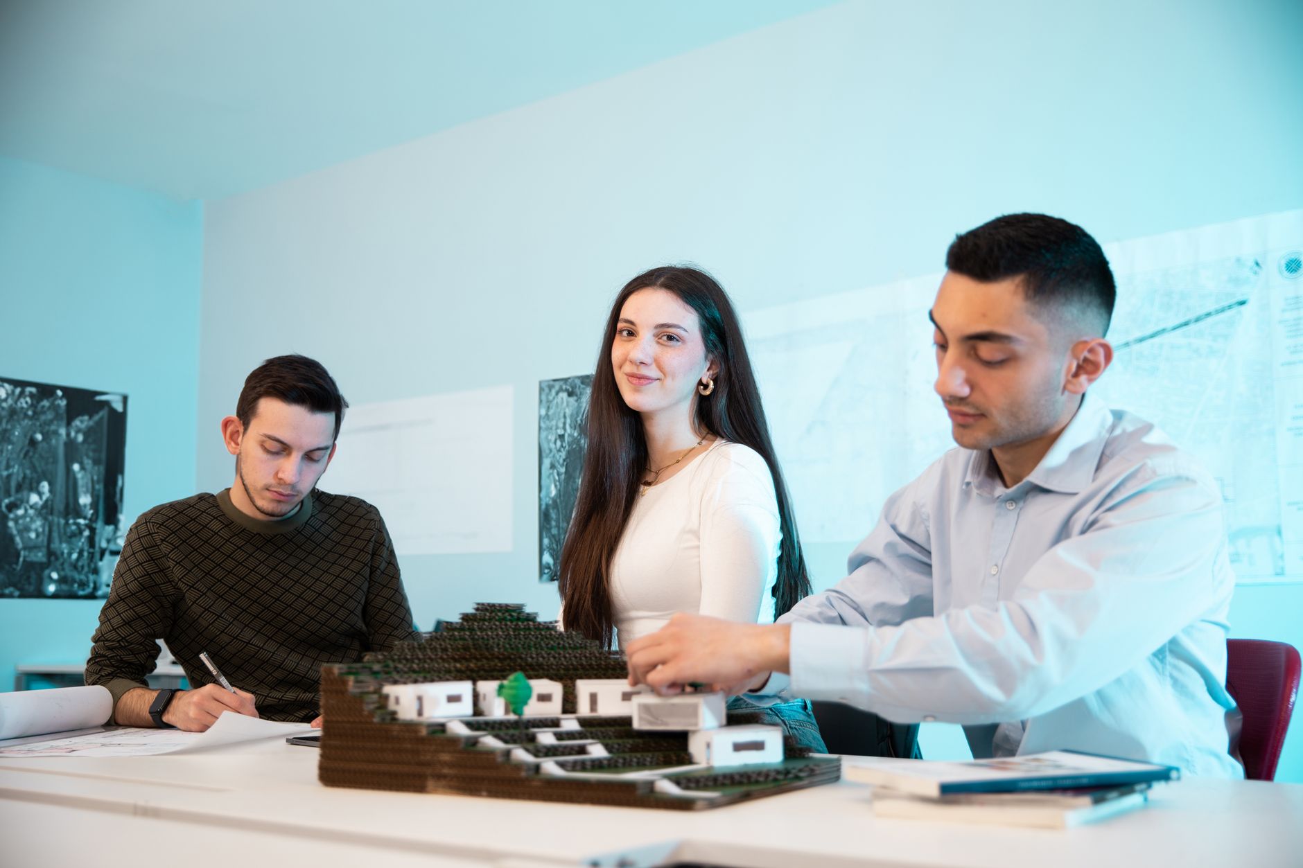 Tres arquitectos jóvenes trabajando sobre una maqueta de edificio en un estudio con planos en la pared