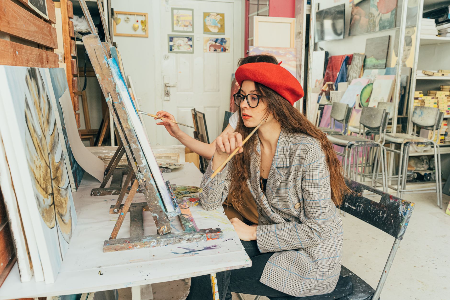 Artista joven pintando sobre un lienzo en un taller lleno de obras