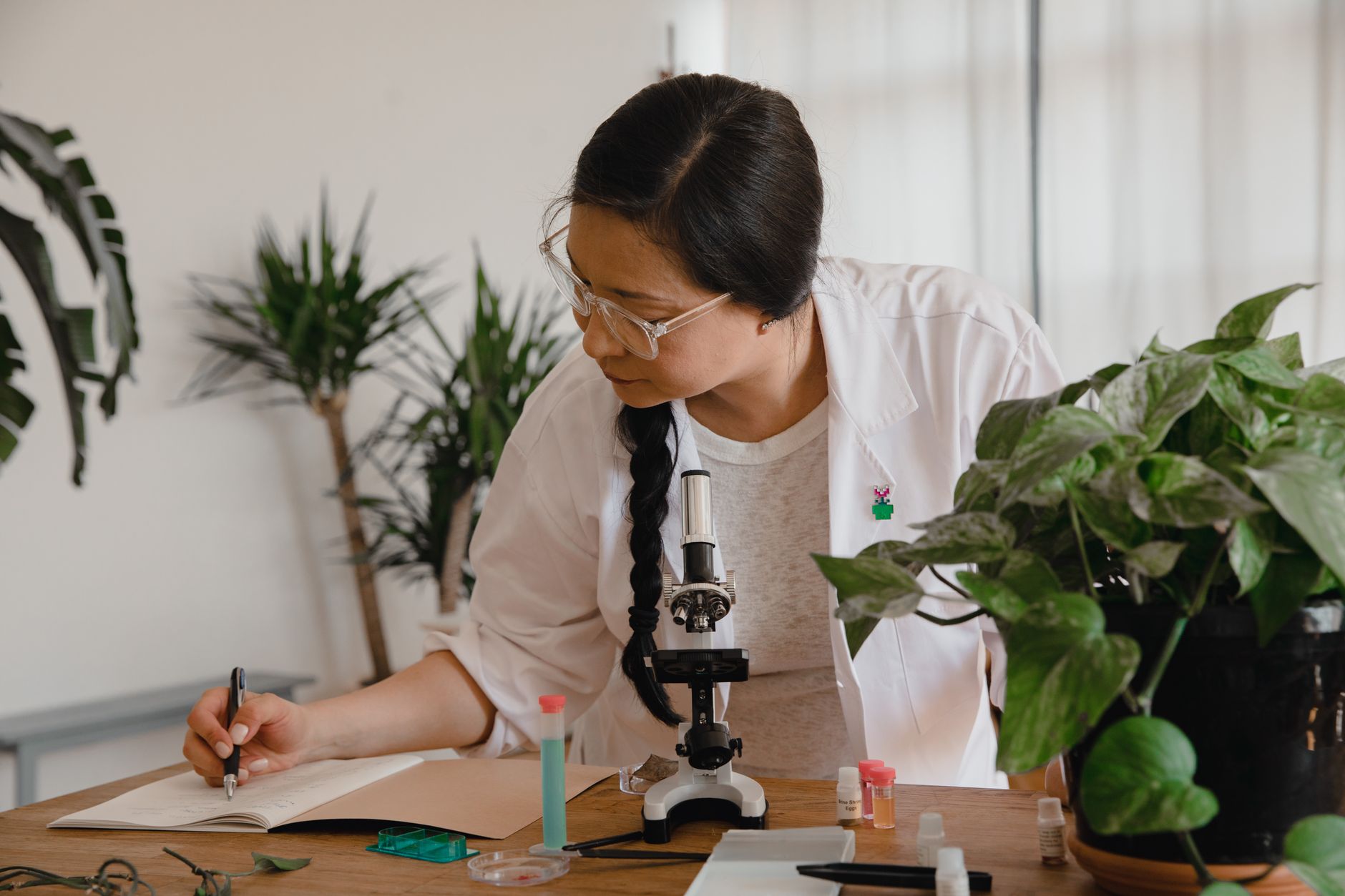 Bióloga joven tomando notas junto a un microscopio en un laboratorio