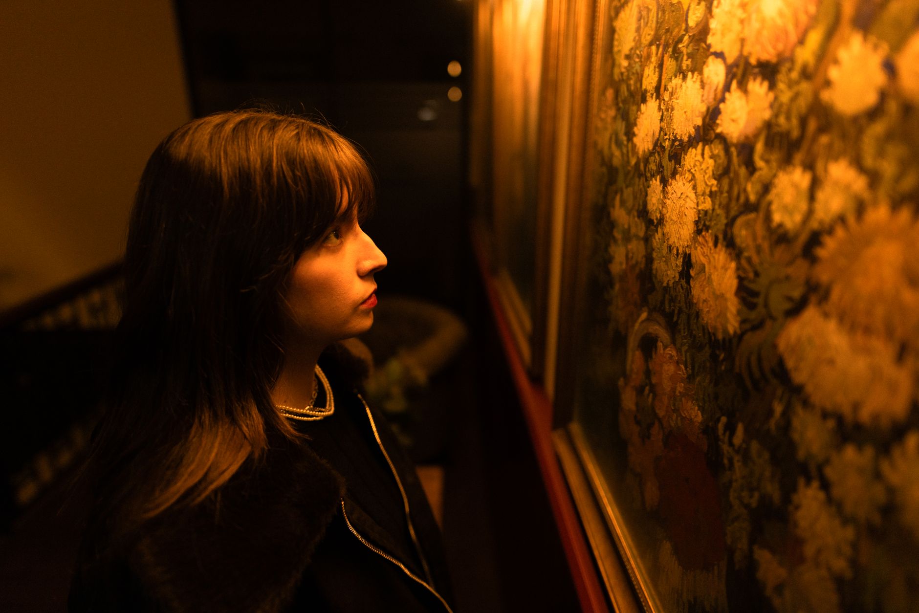 Joven observando de cerca una pintura en una galería de arte